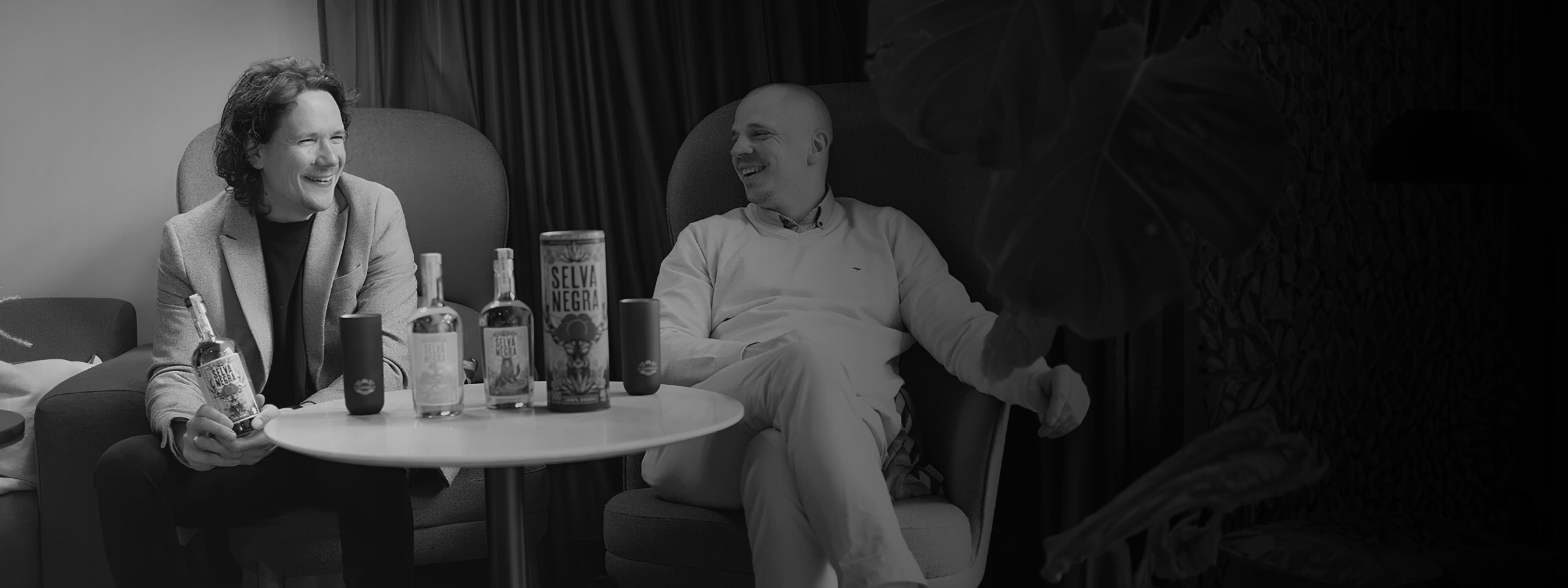 LAURIN LEHMANN UND SEBASTIAN DRESEL LACHEND AN TISCH MIT PRODUKTEN SCHWARZ WEIß